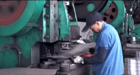 Factory worker stamping making metal half spheres from circular metal sheets